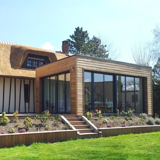 une extension avec baies vitrée et une terrasse au même niveau que l'habitation et aménagement paysager en périphérie