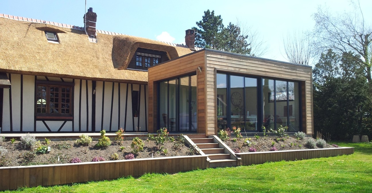 une extension avec baies vitrée et une terrasse au même niveau que l'habitation et aménagement paysager en périphérie